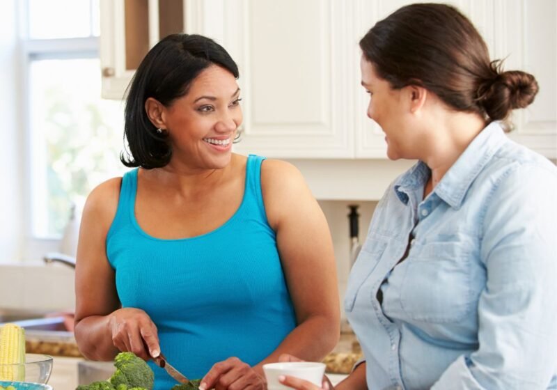 Two women over 40 talking in a kitchen with healthy food